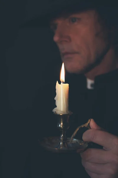 Tajemný viktoriánský kněz v černém kabátě a čepici držící svíčku — Stock fotografie