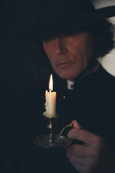 Mysterious victorian priest in black coat and hat holding candle — Stock Photo, Image