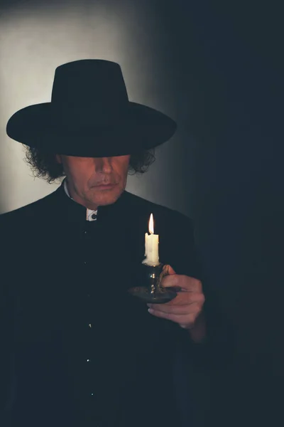 Tajemniczy wiktoriański ksiądz w czarnej sierści i kapeluszu trzymanie świecy — Zdjęcie stockowe