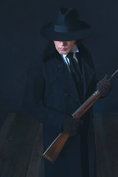Hombre victoriano con abrigo negro largo y sombrero que sostiene el rifle . — Foto de Stock