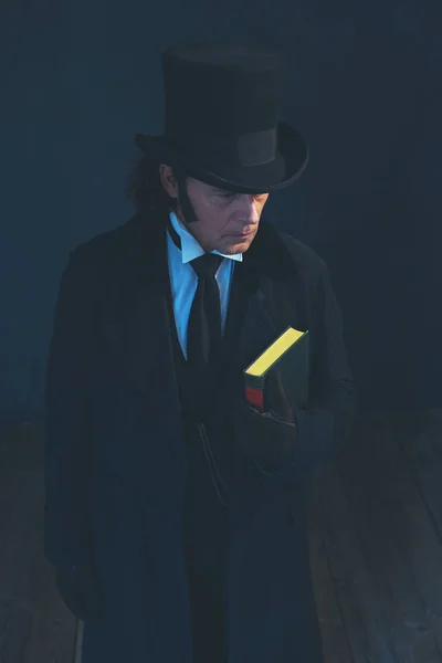 Edwardian man in long black coat and hat holding book. — Stock Photo, Image