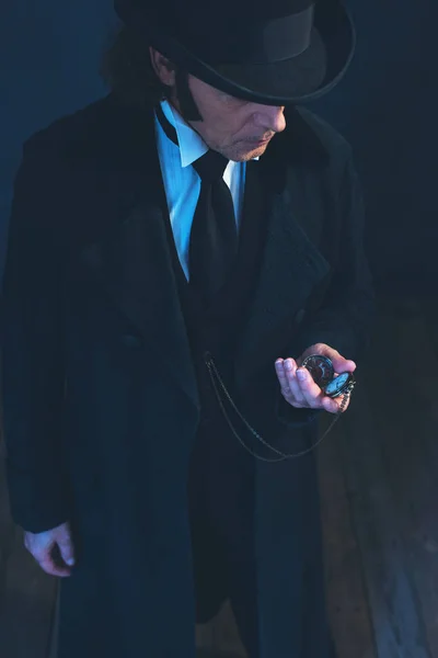 Hombre eduardiano con abrigo largo negro y sombrero sosteniendo reloj de bolsillo . — Foto de Stock