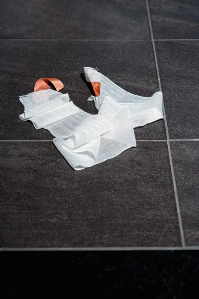 Bandage gauze with tape lying on grey tile floor. Top view. — Stock Photo, Image