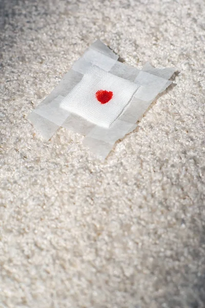 Fallen bandage with blood spot on white carpet.