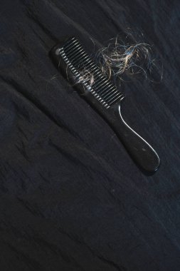 Koyu kumaş üzerinde kıvırcık sarı saçlı siyah tarak.