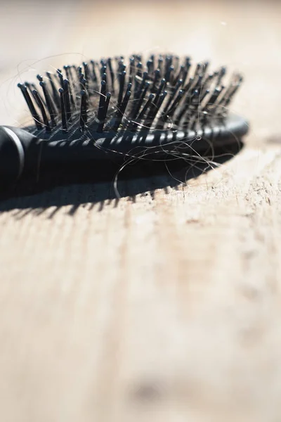 Peigne noir avec cheveux blonds repose sur des planches . — Photo