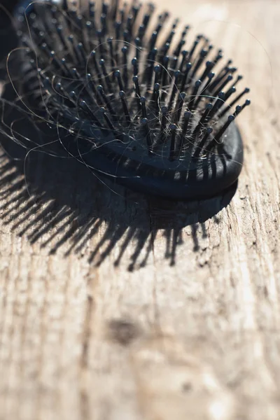 Zwarte haarborstel met blond haar op houten vloer. — Stockfoto