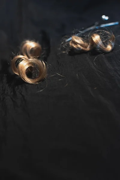 黒い生地にブロンドの巻き毛とはさみの一部. — ストック写真