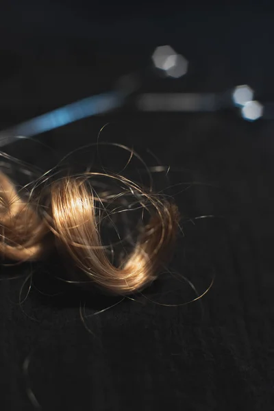 Kawałek blond kręcone włosy i nożyczki na czarnej tkaniny. — Zdjęcie stockowe