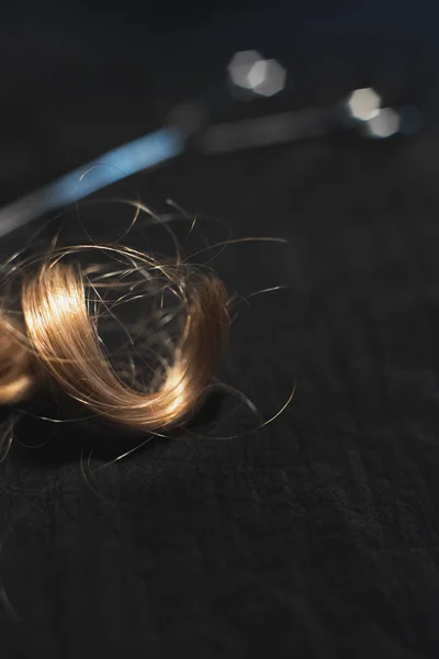 Pedazo de pelo rubio rizado y tijeras en tela negra . — Foto de Stock