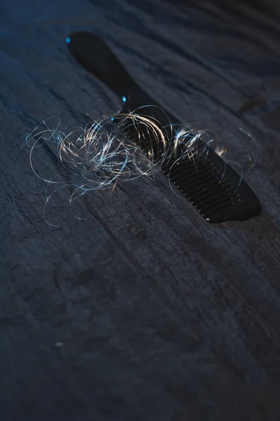 Black comb with curly blonde hairs on dark fabric. — Stock Photo, Image