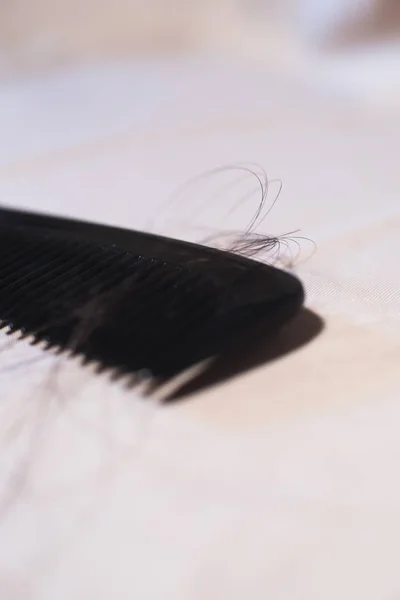 Close-up van zwarte kam met bruine haren op heldere stof. — Stockfoto