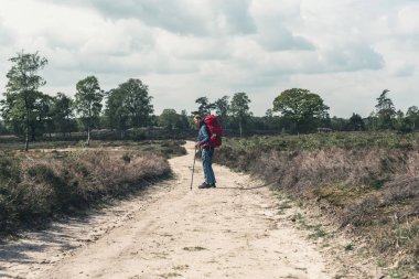 Backpacker bulutlu gökyüzü altında toprak yolda ayakta.