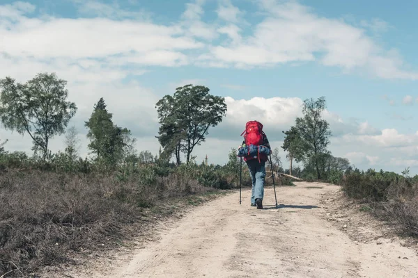 Backpacker går uppför på grusvägen under blå molnigt himmel. — Stockfoto