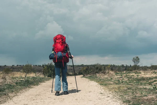 Backpacker går neråt på grusvägen under molnigt himmel. — Stockfoto