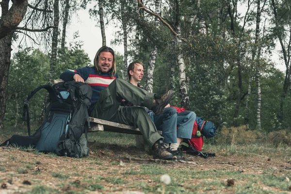 Due backpackers maschili che riposano sulla panchina nella foresta in primavera . — Foto Stock