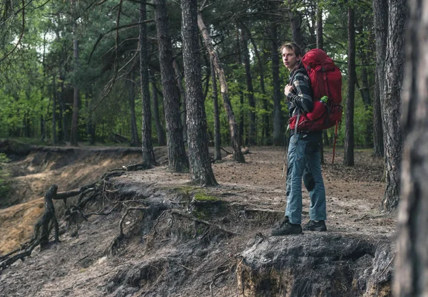 Young man with red backpack at edge of canyon in spring forest. — Φωτογραφία Αρχείου