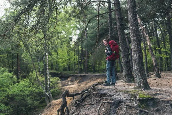 Hombre joven con mochila roja en el borde del cañón en el bosque de primavera . —  Fotos de Stock