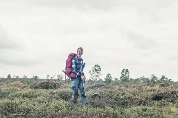 曇り空の下で荒野に立つ笑顔のバックパッカー. — ストック写真