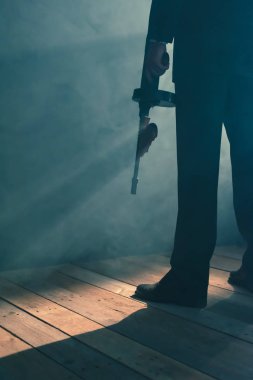 Retro gangster dumanlı odada makineli tüfek ile duruyor. Arka görüş.