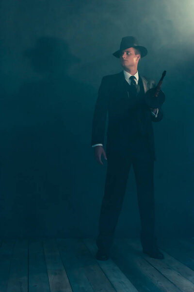 Retro gangster stands with machine gun in smoke.