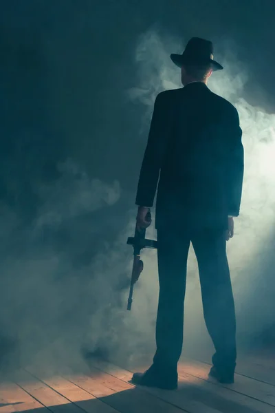 Ретро гангстер стоїть з кулеметом у димній кімнаті. Вид ззаду . — стокове фото