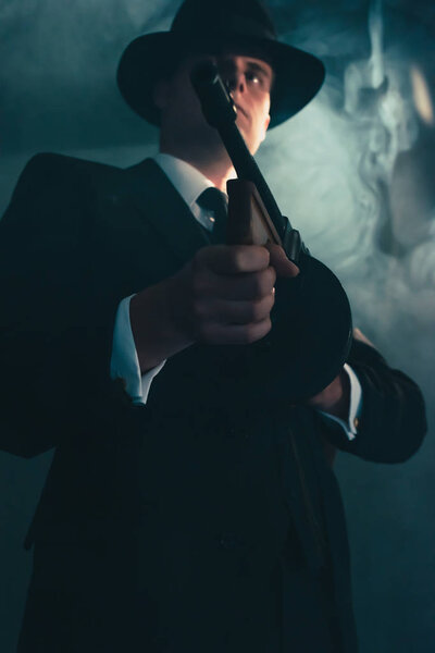 Retro gangster in hat in misty night shoots with machine gun.
