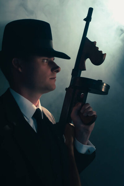 Retro gangster stands with machine gun in mist.