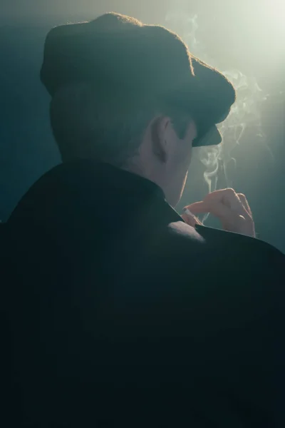 Retro man with cap smokes cigarette in smoky room. Rear view. — Stock Photo, Image