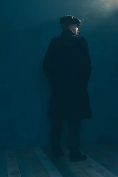 Retro man with cap smokes cigarette in smoky room. Side view. — Stock Photo, Image