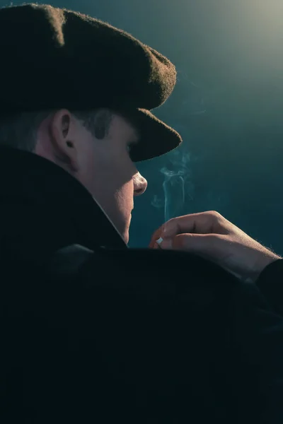 Retro człowiek z czapką pali papierosa w smoky pokoju. Widok z boku. — Zdjęcie stockowe