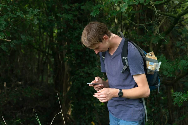 Ung man med ryggsäck i sommar skogen kontrollerar sin smartphone. — Stockfoto