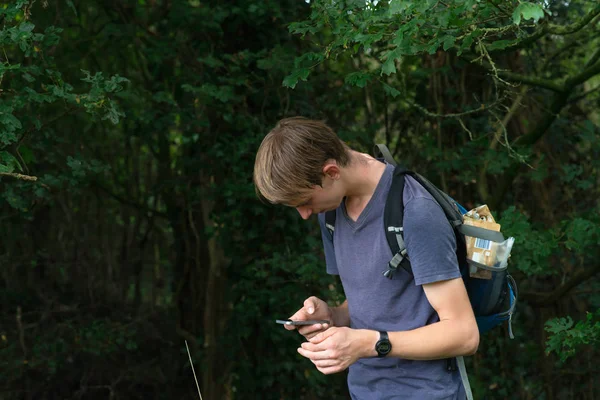 Joven con mochila en el bosque de verano comprueba su smartphone . — Foto de Stock