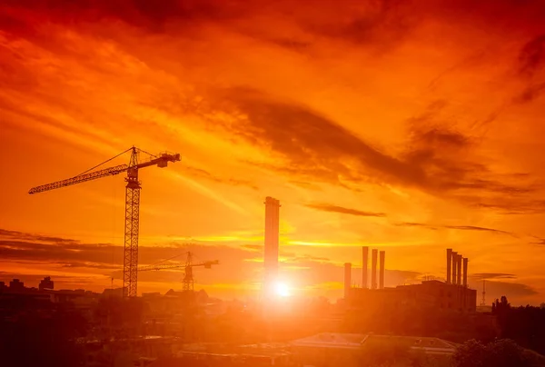 Crane in the construction site under the sunset and city silhouette