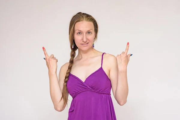 Look here - there is something interesting for you. Portrait of a beautiful woman on a white background showing on a product. She stands right in front of the camera and smiles and looks happy.