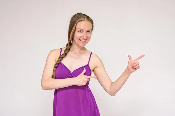 Look here - there is something interesting for you. Portrait of a beautiful woman on a white background showing on a product. She stands right in front of the camera and smiles and looks happy.