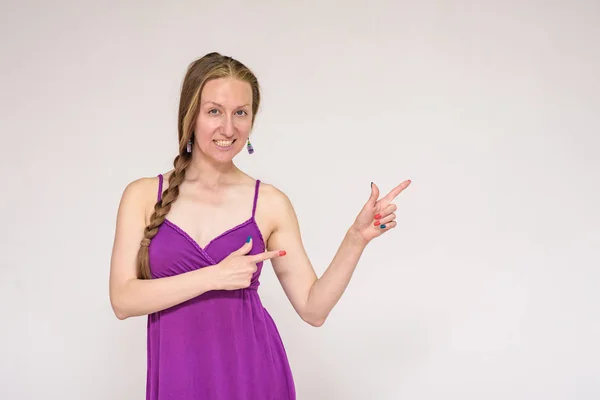 Look here - there is something interesting for you. Portrait of a beautiful woman on a white background showing on a product. She stands right in front of the camera and smiles and looks happy.