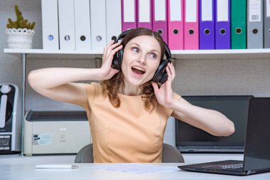 ayın en iyi ofis çalışanı. Bir dizüstü bilgisayar ile kulaklık ile ofiste çalışan güzel bir kızın portresi. Gülümseyen ve mutlu görünüyordu masada oturuyor