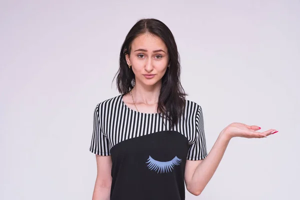 Look Here There is something interesting. Portrait of a beautiful brunette girl in a dress on a white background showing on the product. She is standing right in front of the camera smiling and looking happy