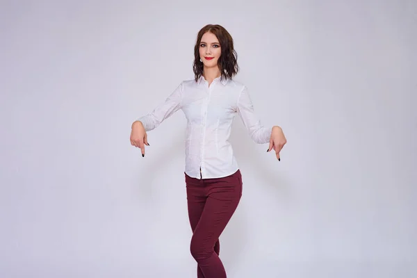 Look here there is something interesting for you. Portrait of beautiful brunette girl on white background showing on product. She is standing right in front of the camera smiling and looking happy