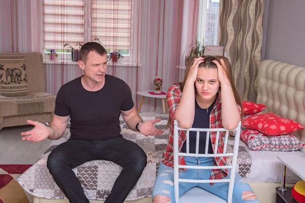 portrait of the father and daughter with family problems, family difficulties in family relationships in the room on the bed. They are right in front of the camera and look unhappy