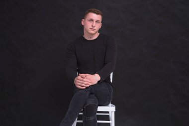 Siyah bir arka planda farklı pozlar sandalyede oturan hoş bir genç adam portresi. O kamera önünde oturur ve ciddi görünüyor