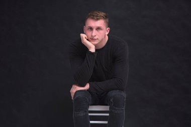 Siyah bir arka planda farklı pozlar sandalyede oturan hoş bir genç adam portresi. O kamera önünde oturur ve ciddi görünüyor