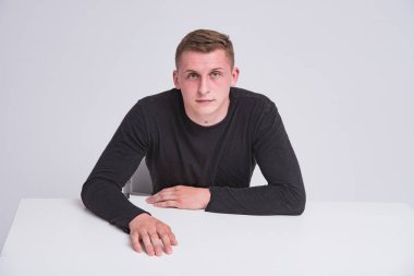 farklı duyguları ile farklı pozlar bir masada oturan beyaz bir arka plan üzerinde hoş bir genç adam portresi. O kamera önünde oturur ve mutlu görünüyor