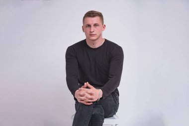 Beyaz bir arka planda farklı pozlar sandalyede oturan hoş bir genç adam portresi. O kamera önünde oturur ve ciddi görünüyor