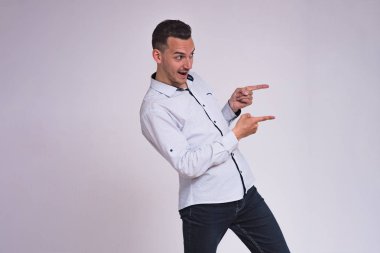 portre sevimli genç esmer adamın beyaz zemin üzerinde bir ürün farklı duygular ile gösterir. Şu kamera gülümseyen önünde duruyor ve mutlu görünüyor