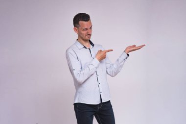 portre sevimli genç esmer adamın beyaz zemin üzerinde bir ürün farklı duygular ile gösterir. Şu kamera gülümseyen önünde duruyor ve mutlu görünüyor