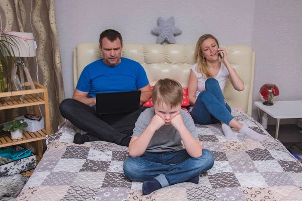 portrait of husband and wife and son aged 6 years in the room: family difficulties, problems, family relationships. They sit in front of the camera to quarrel and look unhappy