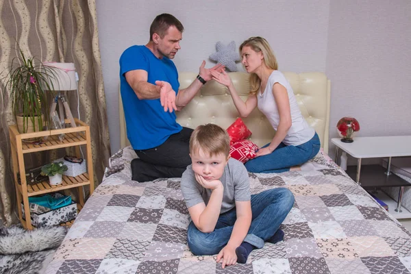 portrait of husband and wife and son aged 6 years in the room: family difficulties, problems, family relationships. They sit in front of the camera to quarrel and look unhappy