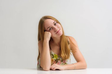 Stüdyo portre fotoğraf gülümseyen güzel bir kızın uzun saçlı duygularla bir masada oturan konuşuyor. O çeşitli pozlar kamera önünde duruyor ve mutlu görünüyor.